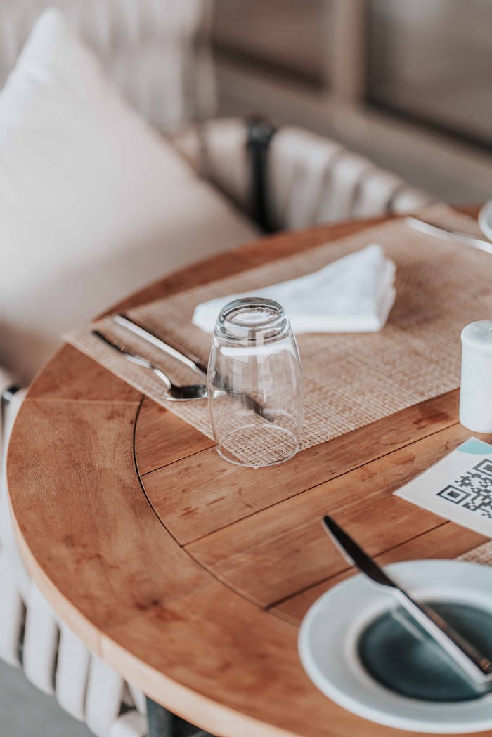 A wooden table set for dining outdoors with a glass, fork, and QR code menu option.