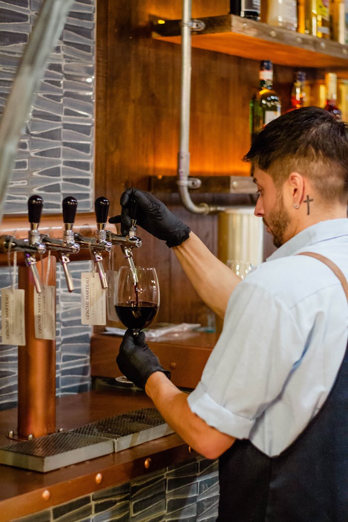 A skilled bartender pours red wine into a glass at a trendy, modern bar.