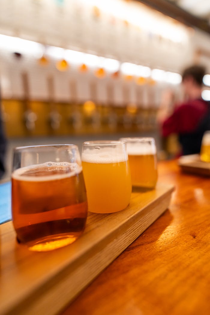 A wooden tray with a flight of craft beers in various colors on a pub table.