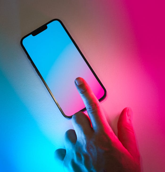 A hand interacts with a glowing smartphone screen in a neon-lit setting, featuring vibrant gradient colors.